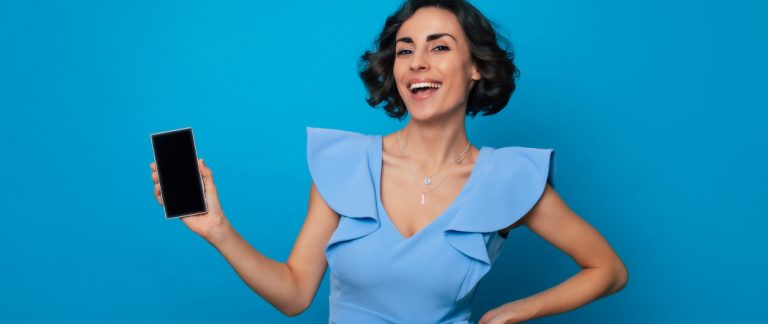 Mulher sorri enquanto mostra o celular.