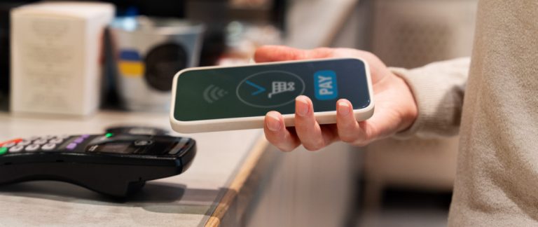 Close em uma pessoa aproximando o celular da máquina de cartão para realizar um pagamento.