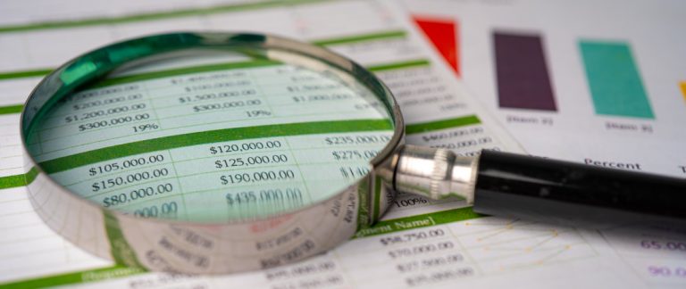 Lupa sobre uma planilha financeira com números e gráficos coloridos ao fundo, representando análise de crédito ou avaliação financeira.