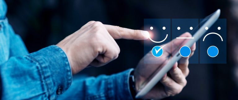 Pessoa usando tablet para selecionar opção de avaliação positiva com ícone de rosto sorridente.