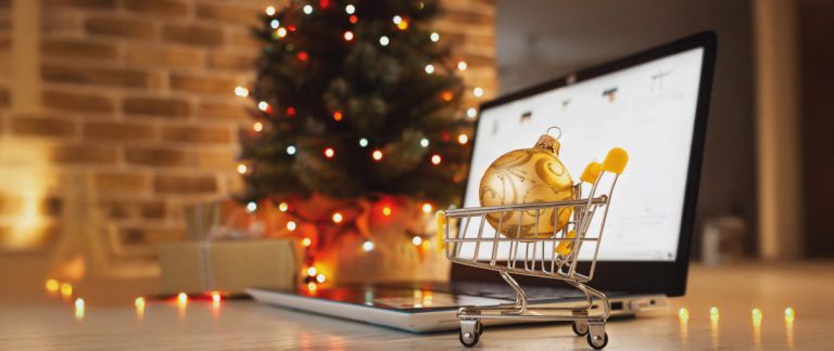 Carrinho de compras em miniatura com bola de Natal dourada sobre notebook, simbolizando vendas online e estratégias para vender mais no Natal.
