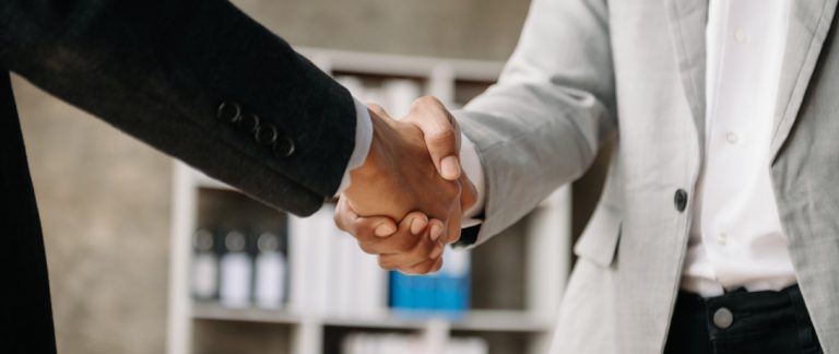 Duas pessoas de terno apertando as mãos em ambiente corporativo, simbolizando a retomada de relacionamento com clientes inativos.